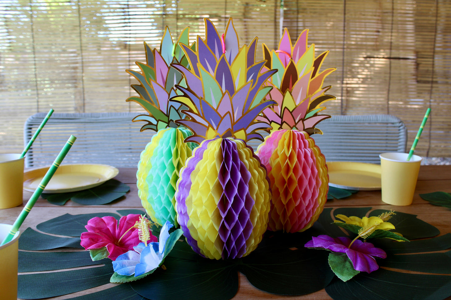 Au centre, il y a trois grandes monstera posées en quinconce, avec au dessus trois ananas en papier pliables. Un est jaune et bleu turquoise, un autre violet et jaune, et enfin le troisième est rose et jaune. Autour de ces ananas il y a quatre fleurs tropicales artificielles de différentes couleurs.